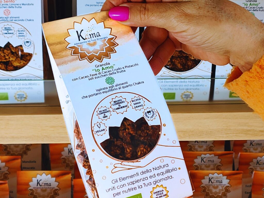 Confezione di granola Kama Holistic Bakery scelta a mano da uno scaffale, prodotti artigianali vegan, senza grano e low carb.