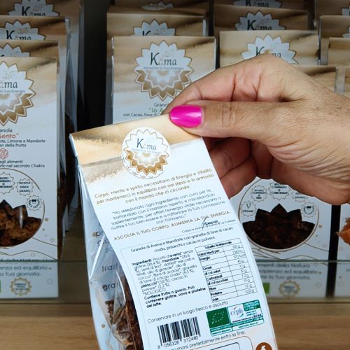 Mano femminile legge l'etichetta nutrizionale di un prodotto Kama sullo scaffale, simbolo di una scelta consapevole e informata.